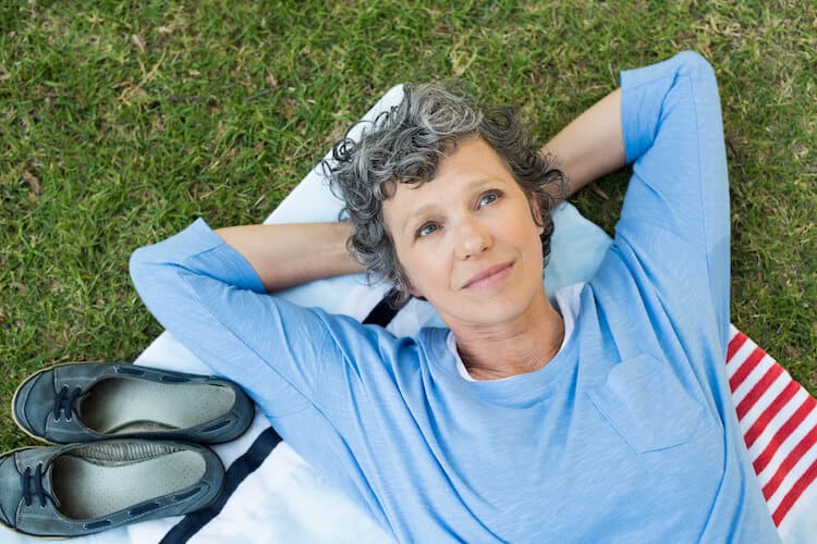 A senior woman lying on a blanket in the grass, contemplative.