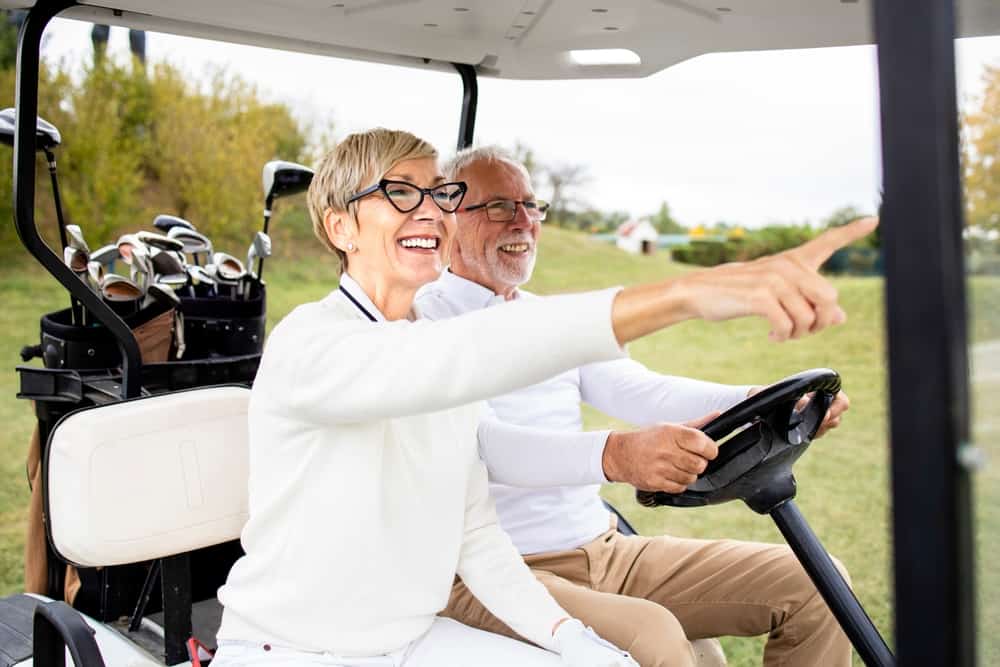 A senior woman and senior man in a golf cart on a golf course