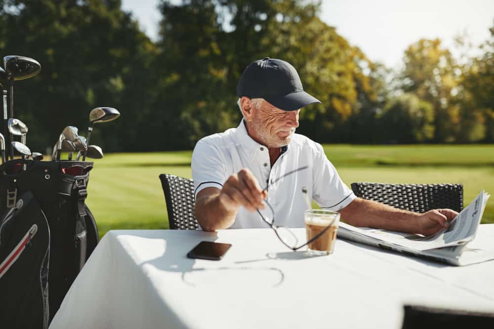 A man reads the newspaper while sitting outside at the golf course