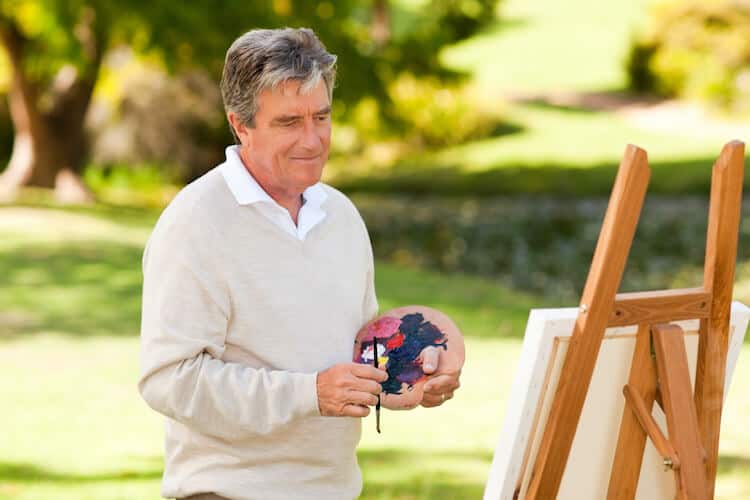 A senior man enjoying summer activities for seniors by painting outdoors.
