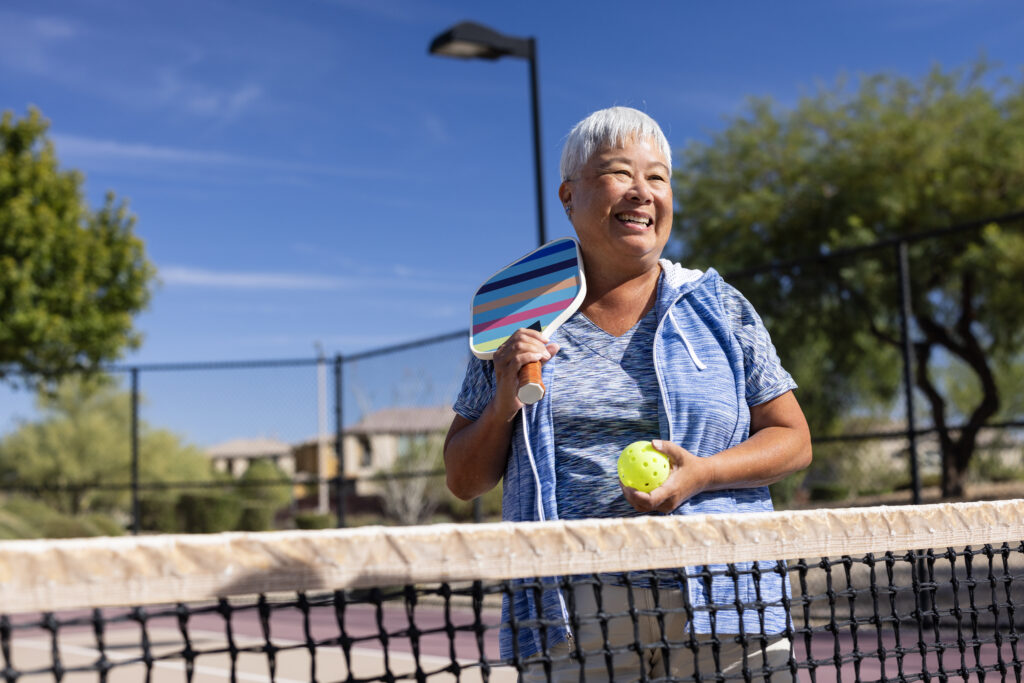 A senior woman having fun playing pickleball at the park.