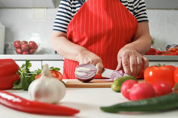 Senior woman cooking using fresh vegetables.
