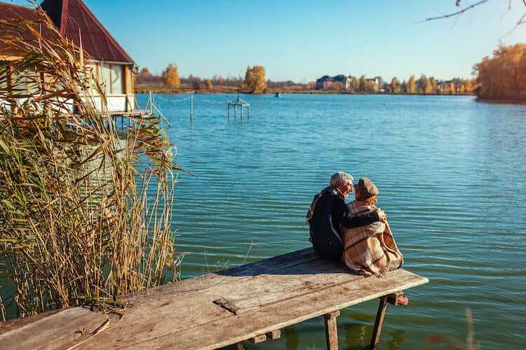 A senior couple relax on a dock by a lake.