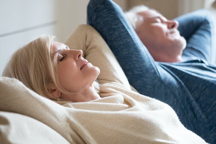 A senior couple practicing meditation together on a couch.