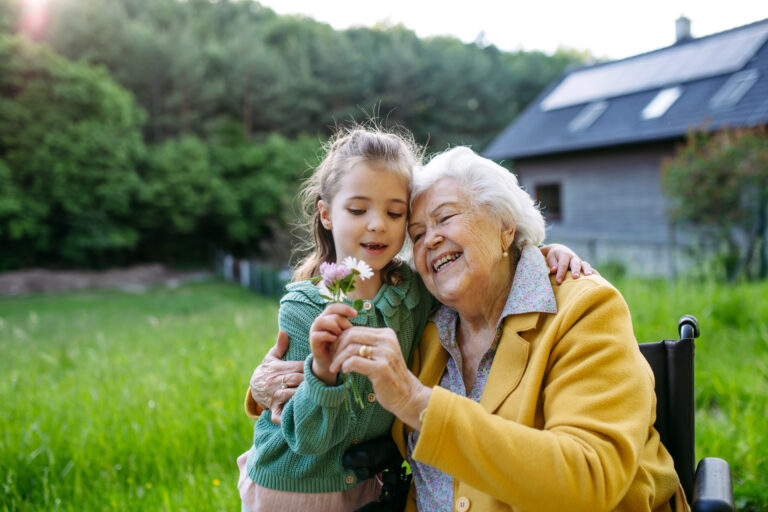Granddaughter spending time with elderly grandma, picking widlflowers. Senior lady in wheelchair spending time in nature.