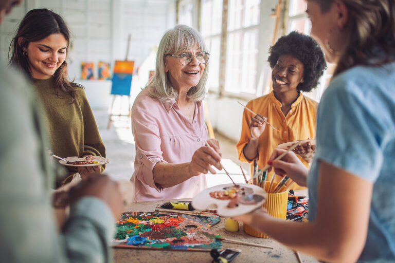 Smiling art school teacher instructs a diverse group of students practicing canvas