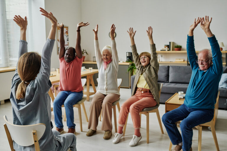 Group of senior people sitting on chairs and exercising during sport training with instructor