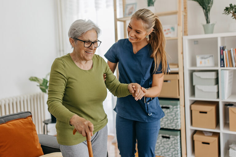 Senior woman with cane being helped by woman in scrubs