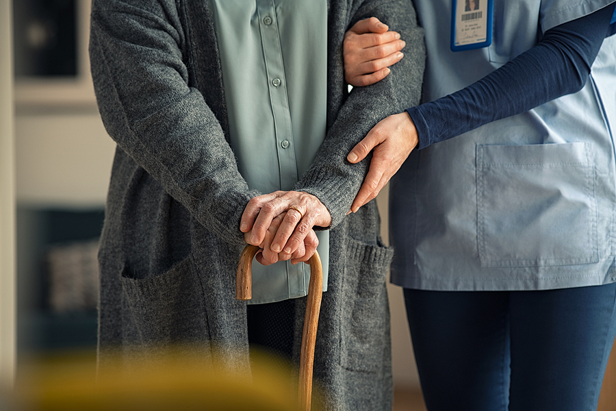 Close up hands of caregiver doctor helping old woman at clinic. Nurse holding a senior patient with walking stick. Elder woman using walking cane at nursing home with nurse holding hand for support.