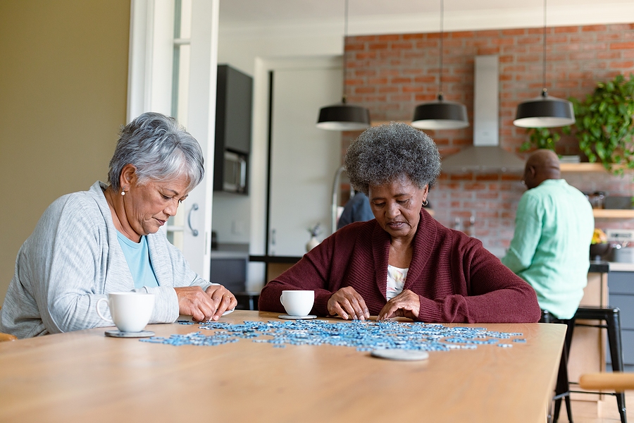 Senior friends sitting in kitchen with coffee and doing puzzles.