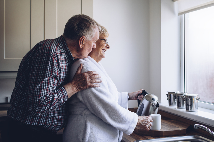 A senior man hugging a senior woman as she makes tea