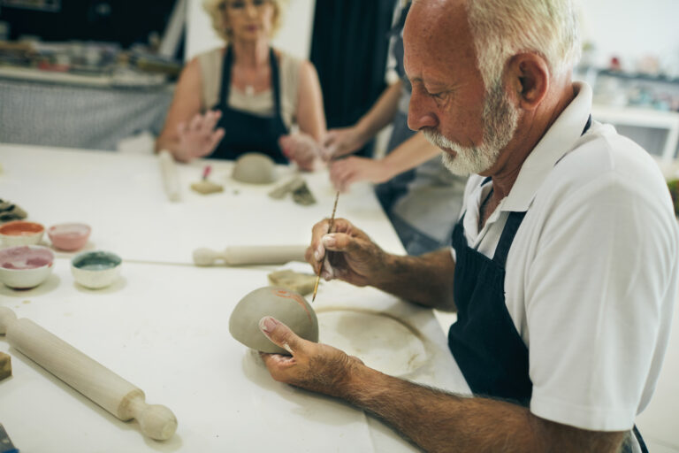 Senior man at ceramics workshop decorating bowl.