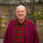Senior man in red plaid shirt smiling for a photo outside
