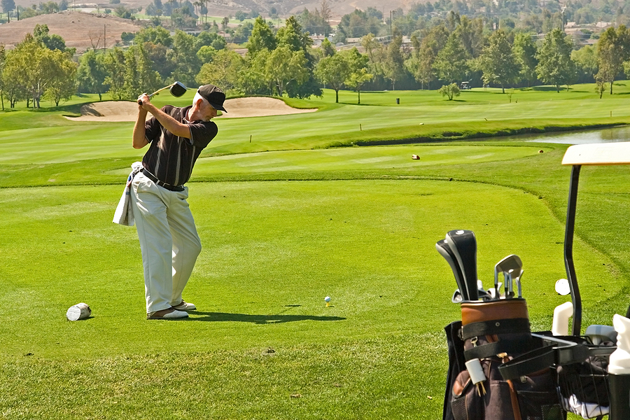 A senior man is out golfing, swinging his golf club on a course
