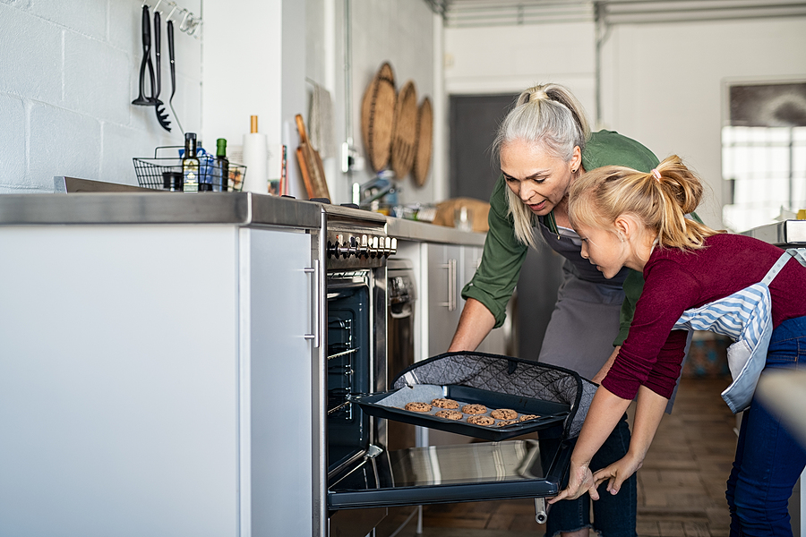 Grandmother and granddaughter are pulling cookies out of the oven.