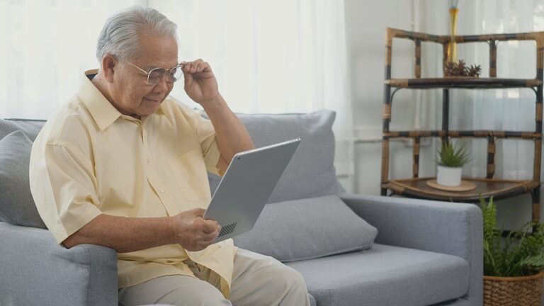 Senior man stting on sofa looking news on digital tablet computer in living room at home