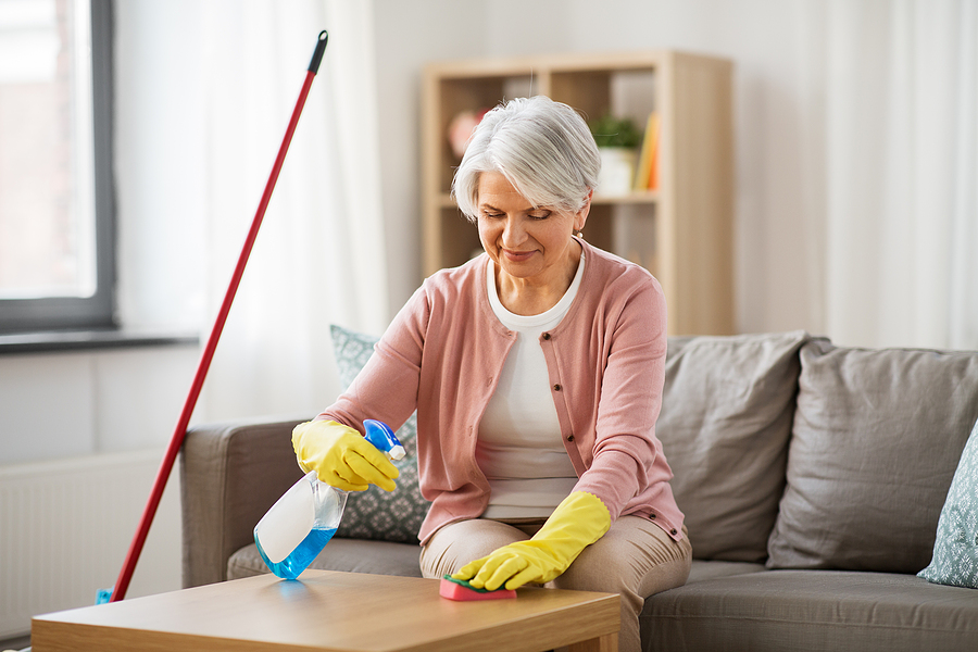 A senior woman wears gloves and cleans a coffee table